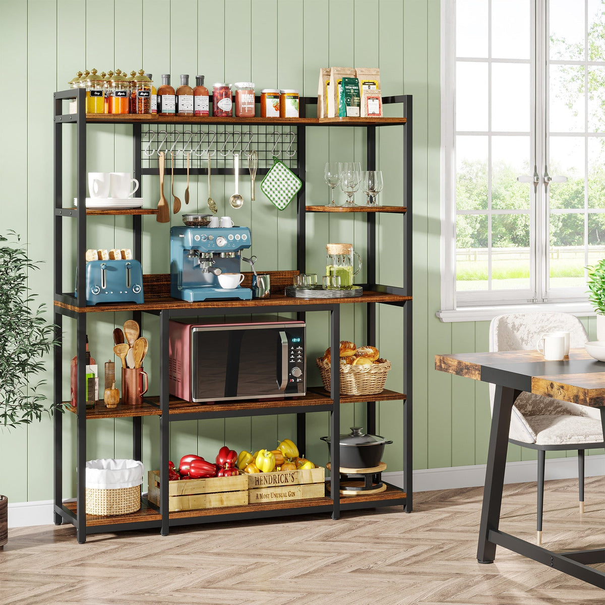 Bakers rack against a green wall stocked with crockery, bottles and a microwave