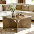 Stowena 31.5 inch square farmhouse coffee table in light oak with a vase and books by a sectional