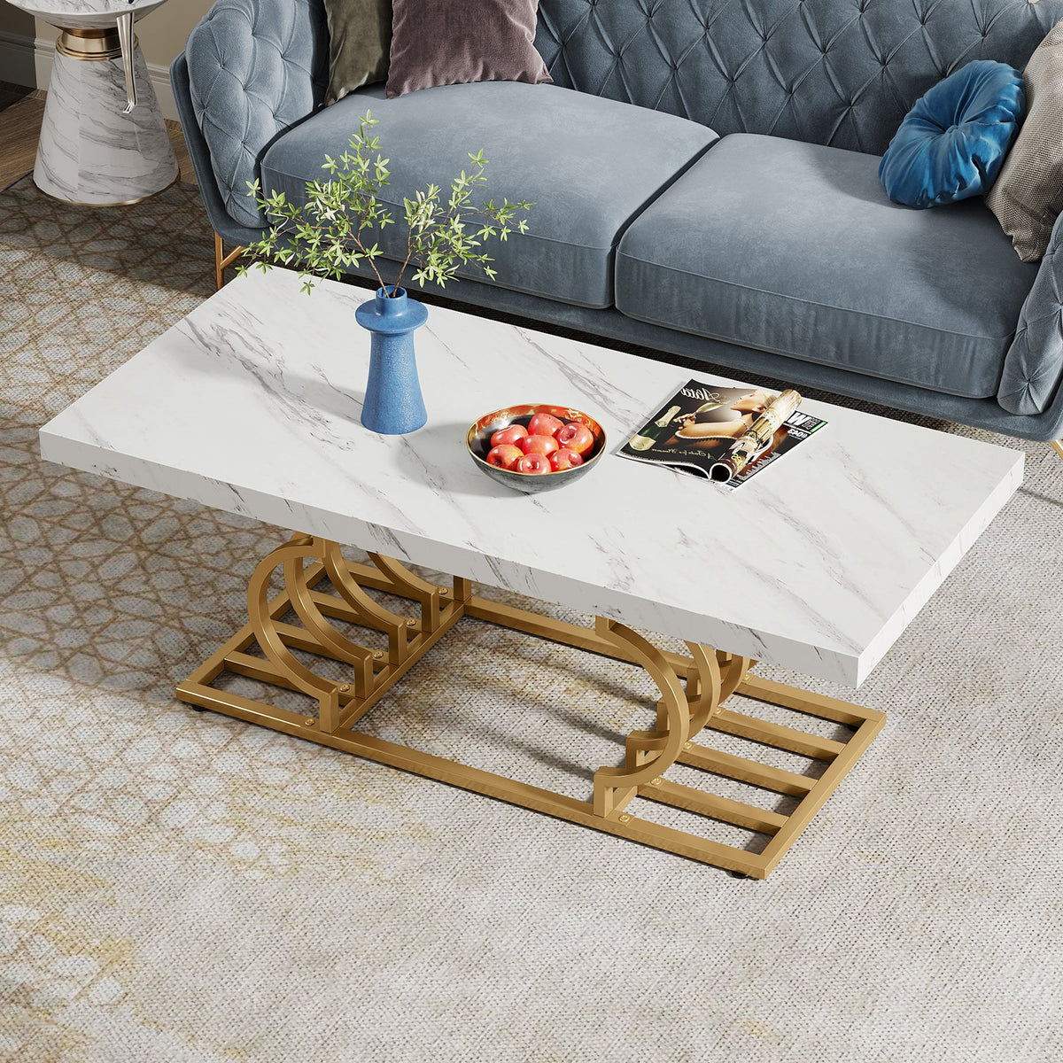Marble look coffee table with a blue vase and fruit bowl beside a blue tufted sofa