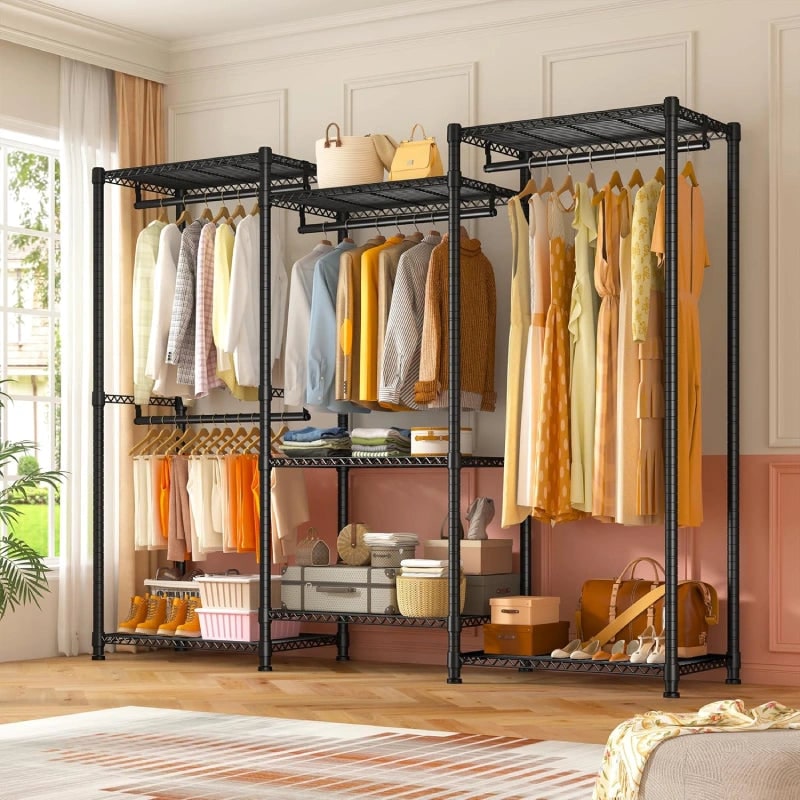 Black closet rack in a bedroom beside a curtained window, holding hanging clothes, folded stacks and a woven basket