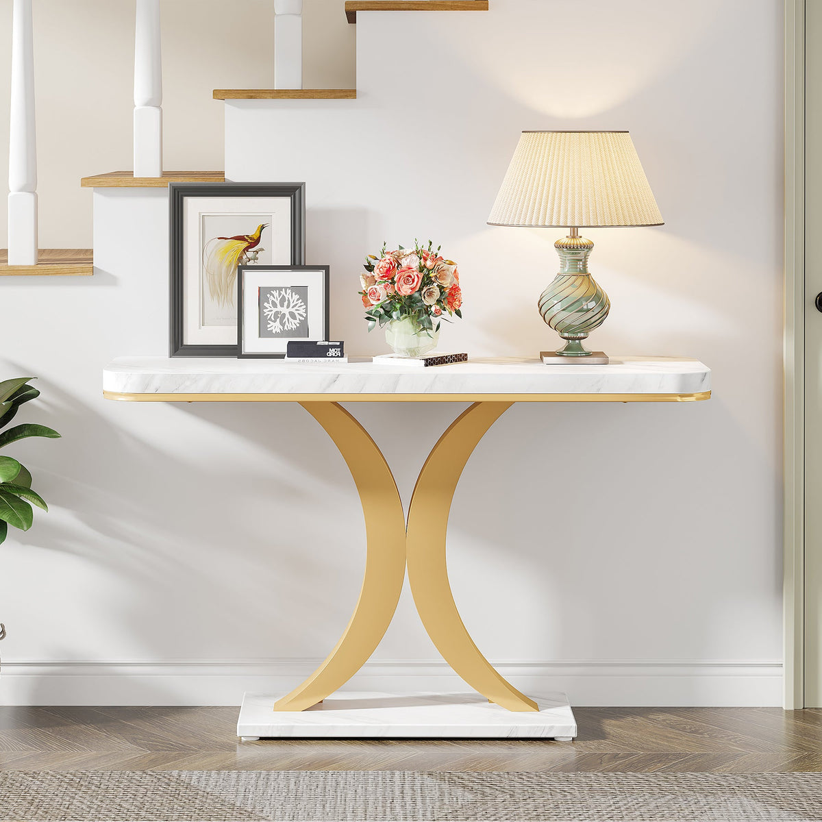 The white and gold console in a hallway beside a staircase with a lamp and framed pictures