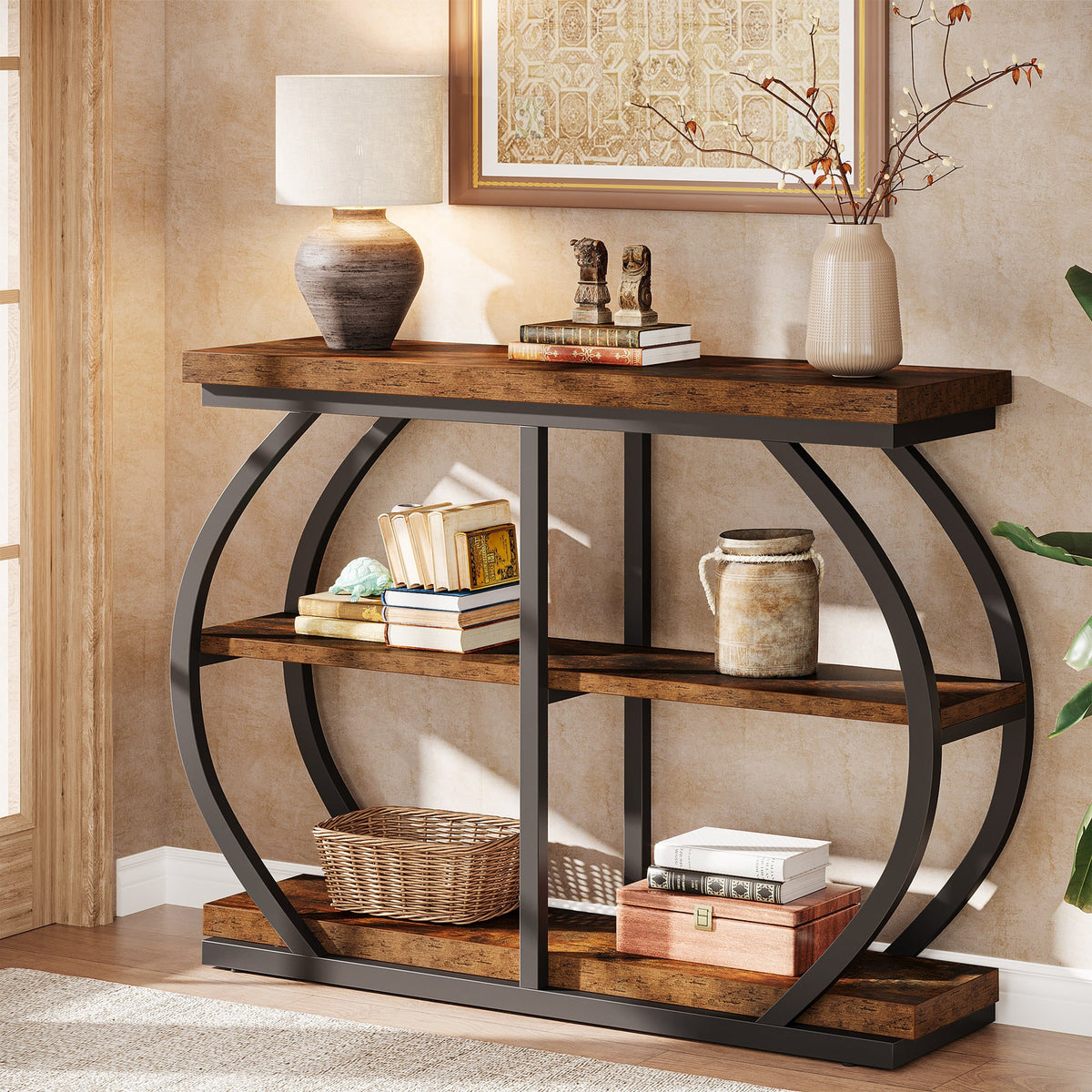 Brown three tier console table in a hallway with a lamp, books and baskets across its shelves
