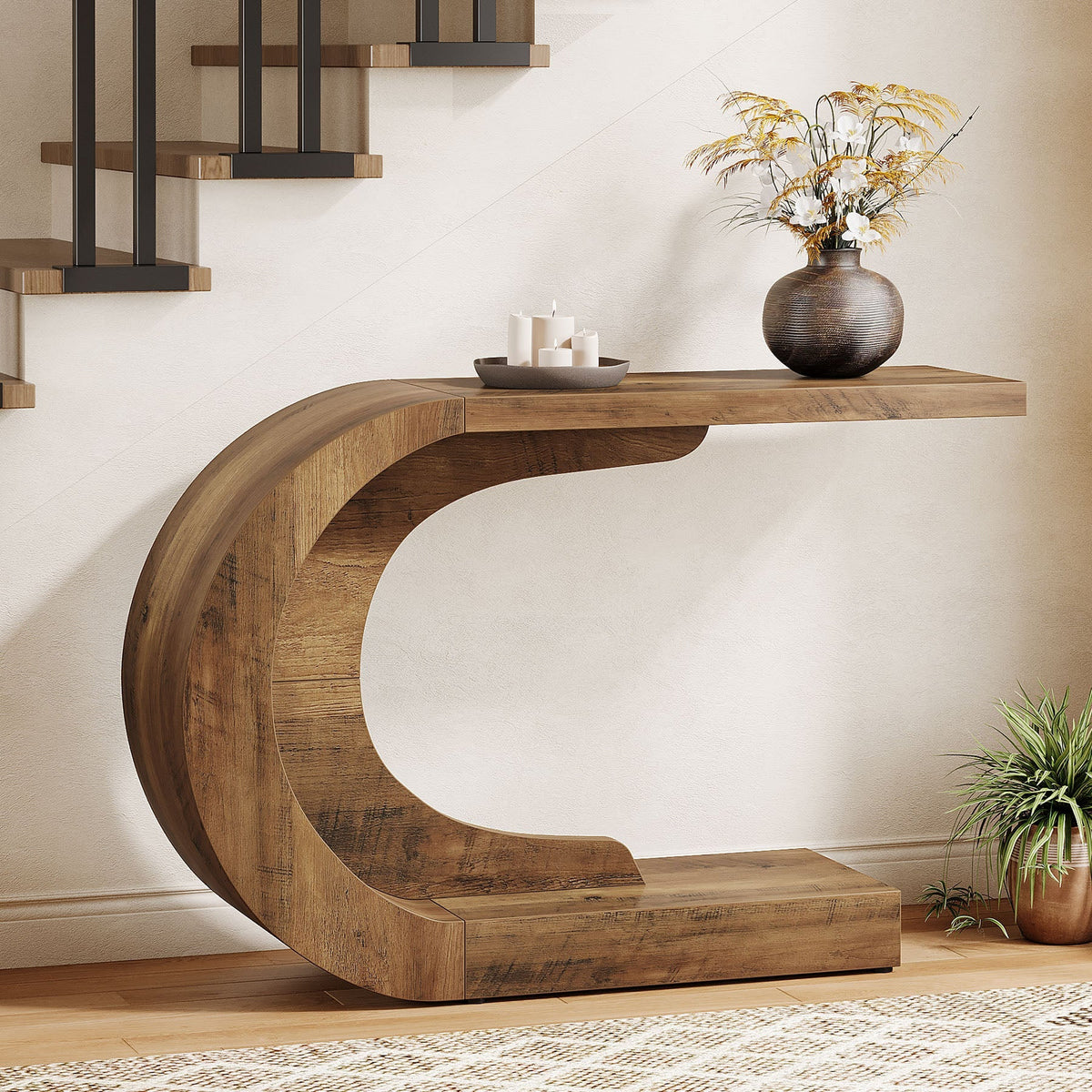 Rustic brown C shaped console table beside a staircase holding a vase and candles