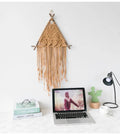 Khaki macrame wall hanging on wood branches above a desk, view 1