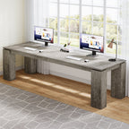 Two monitors side by side on the continuous gray desktop by a window