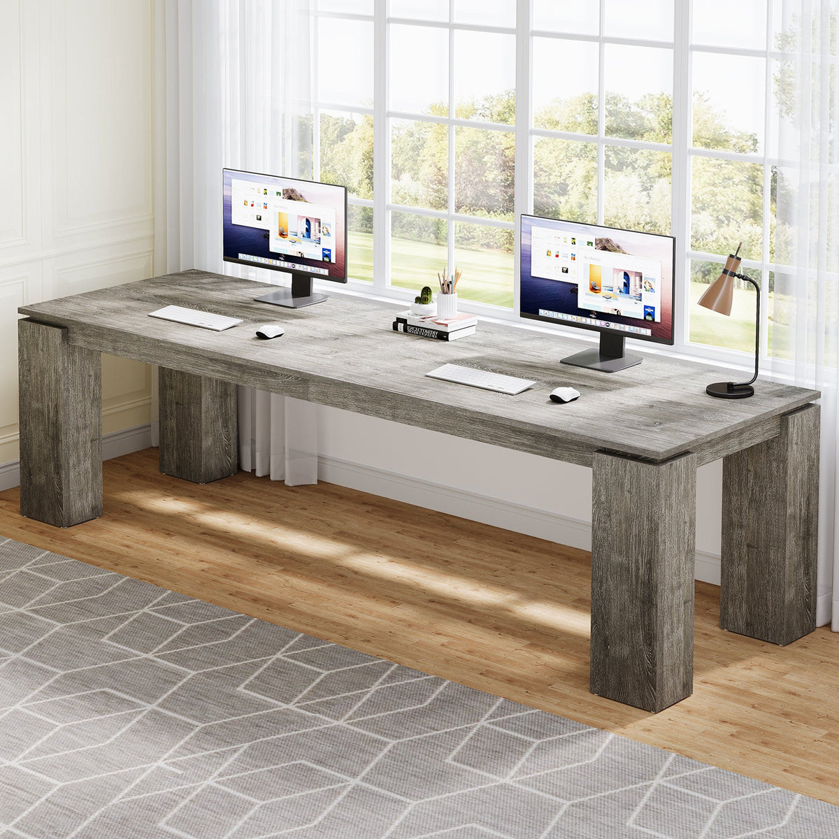 Two monitors side by side on the continuous gray desktop by a window