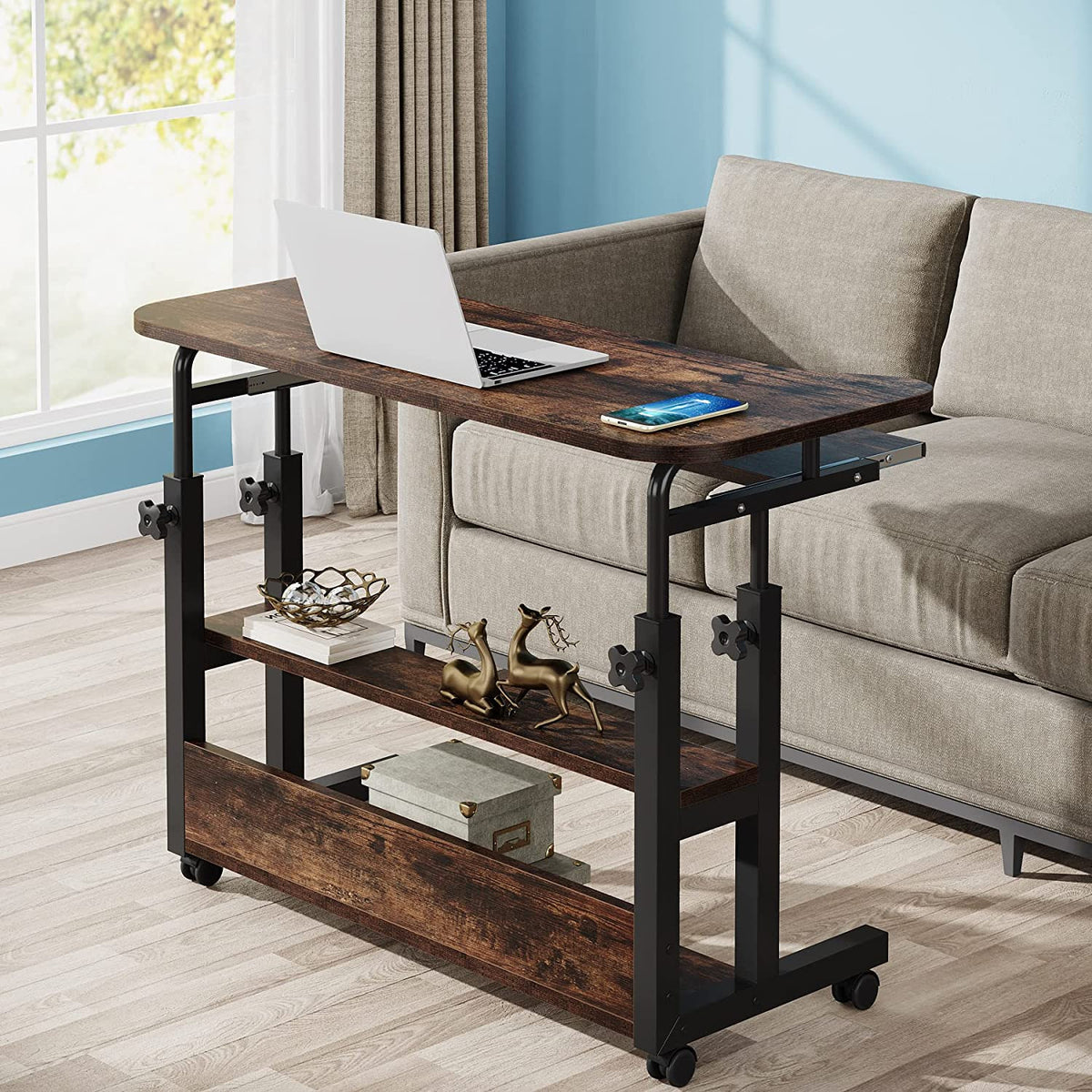 Brown mobile height adjustable desk rolled over a sofa with a laptop on the surface