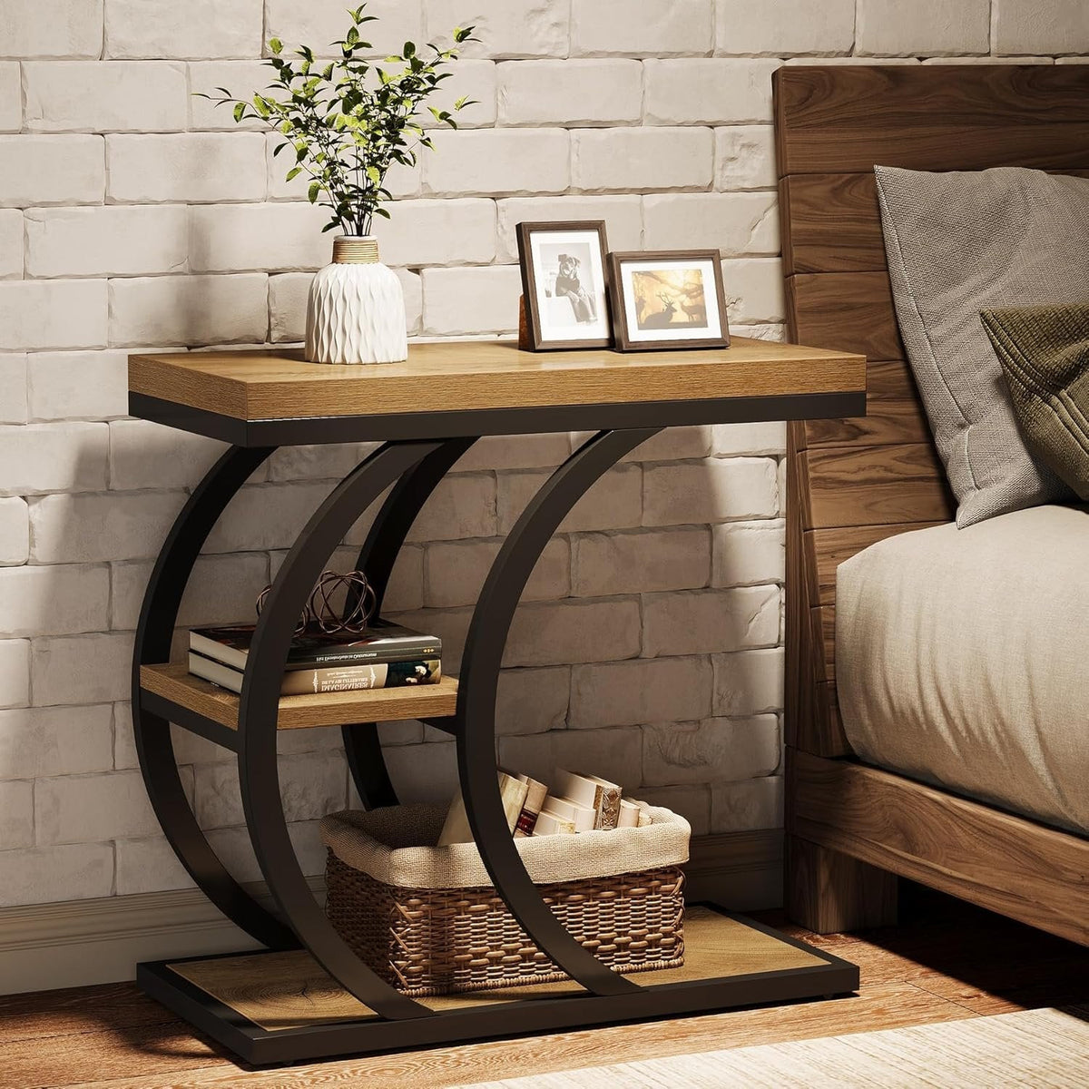 C shaped side table beside a bed holding photo frames and a vase