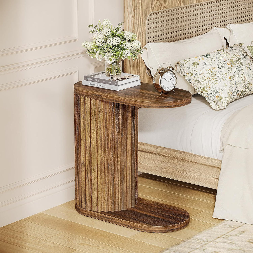 Fluted end table beside a bed with a vase and books on top