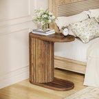 Fluted end table beside a bed with a vase and books on top