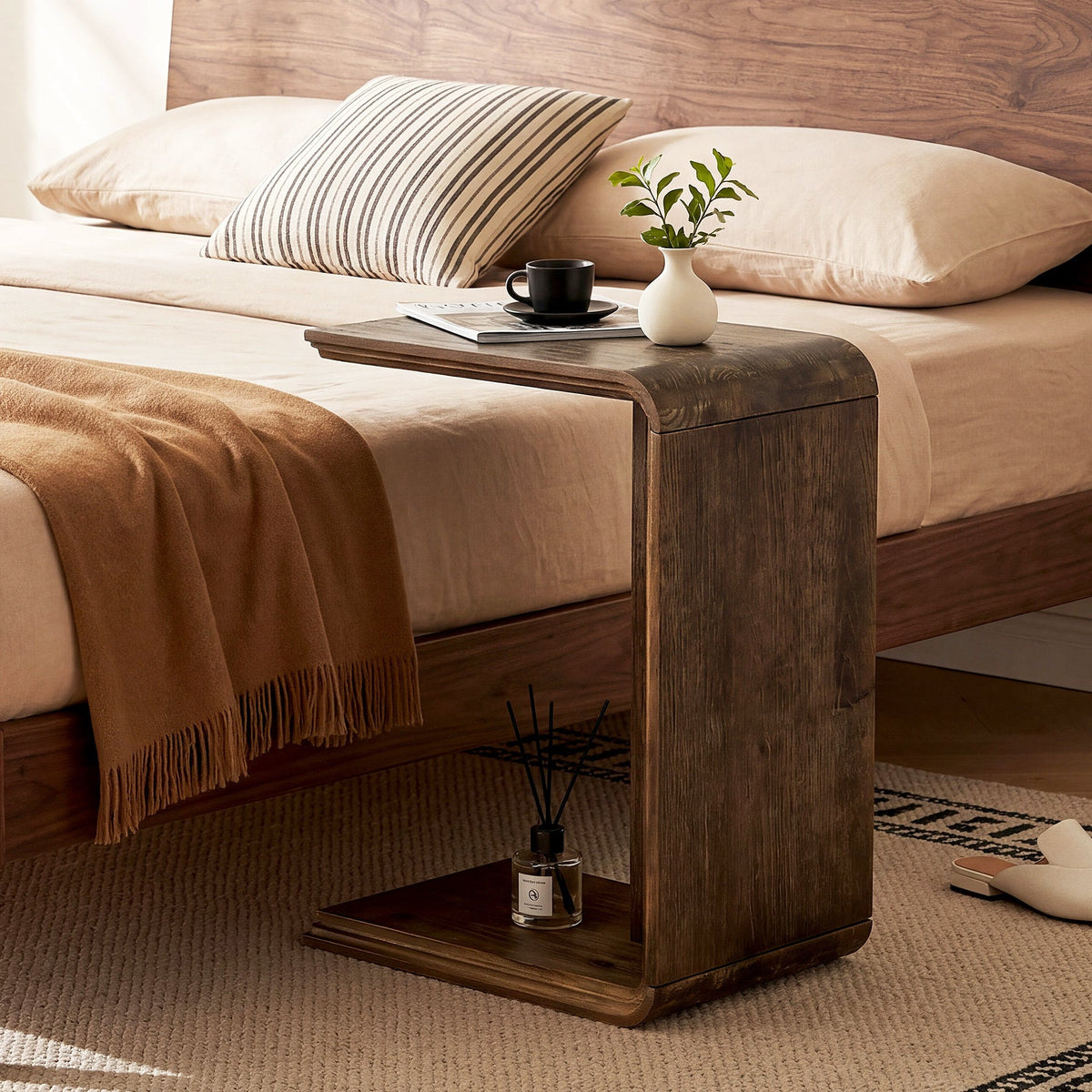 C shaped table serving the bedside over a wooden bed frame with a coffee cup