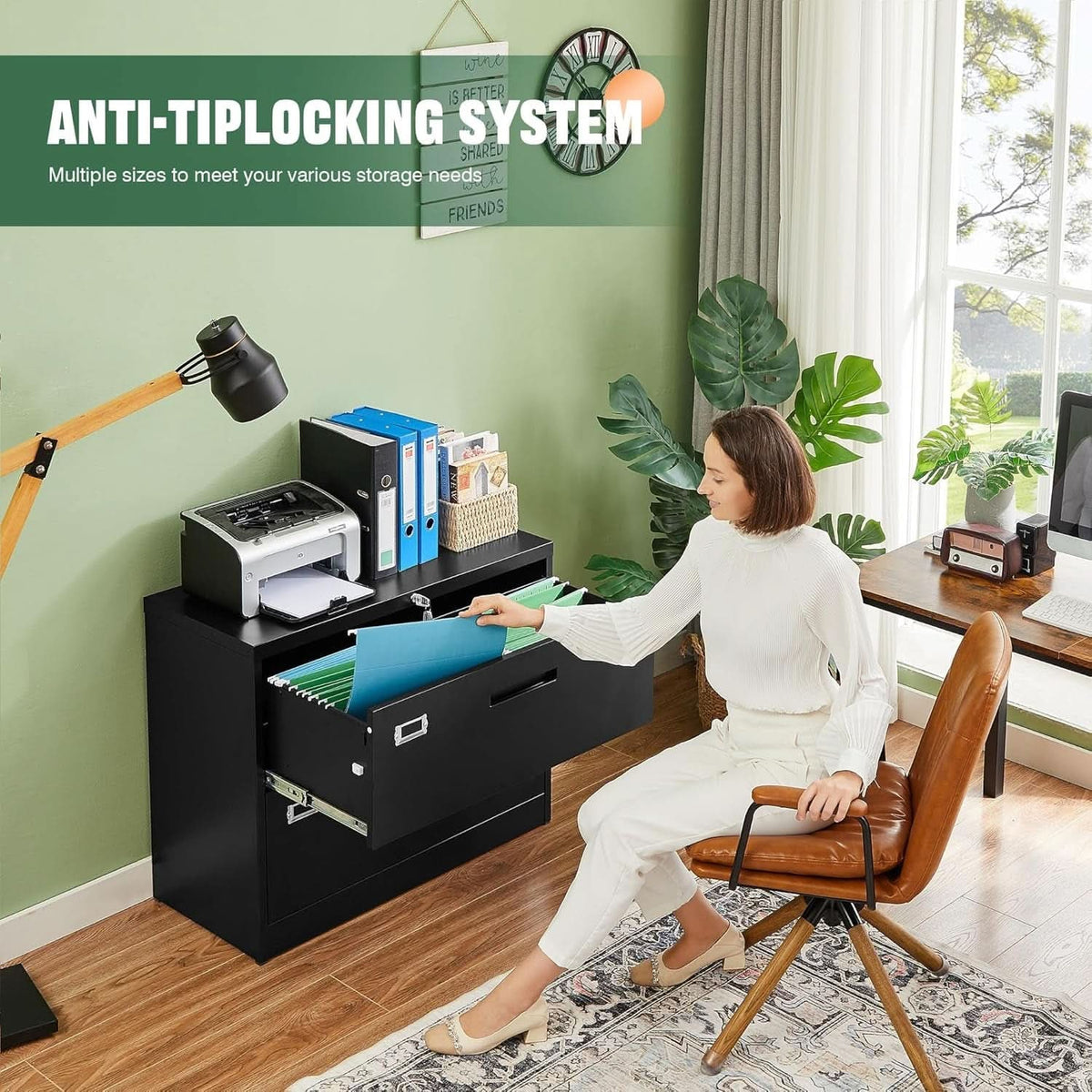 Black 2 drawer lateral file cabinet beside a desk in a green home office, lower drawer open with hanging files