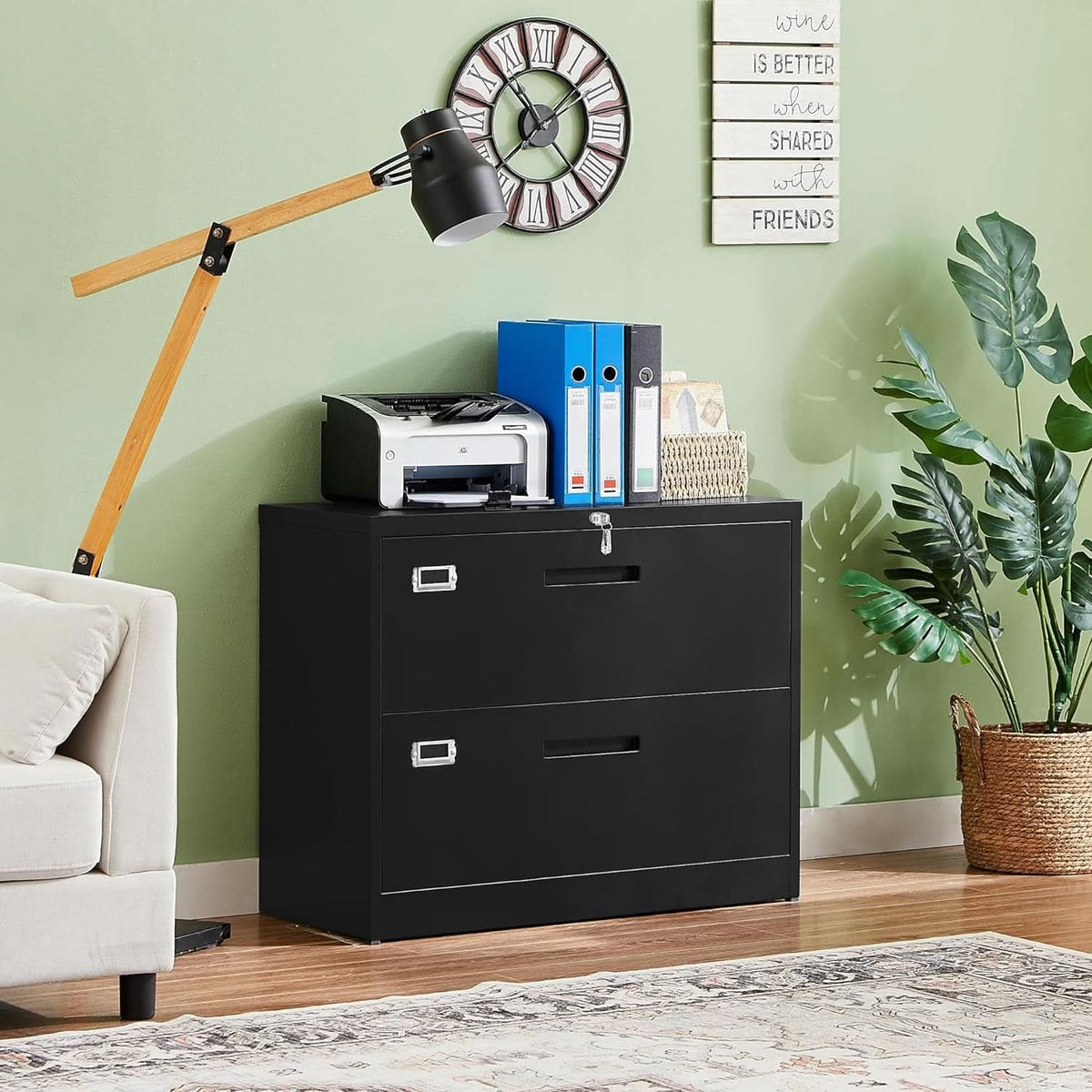 Black lateral file cabinet against a green wall holding a printer, binders and a potted plant