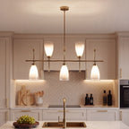 The brass chandelier lit above a kitchen island with a herringbone tiled wall behind
