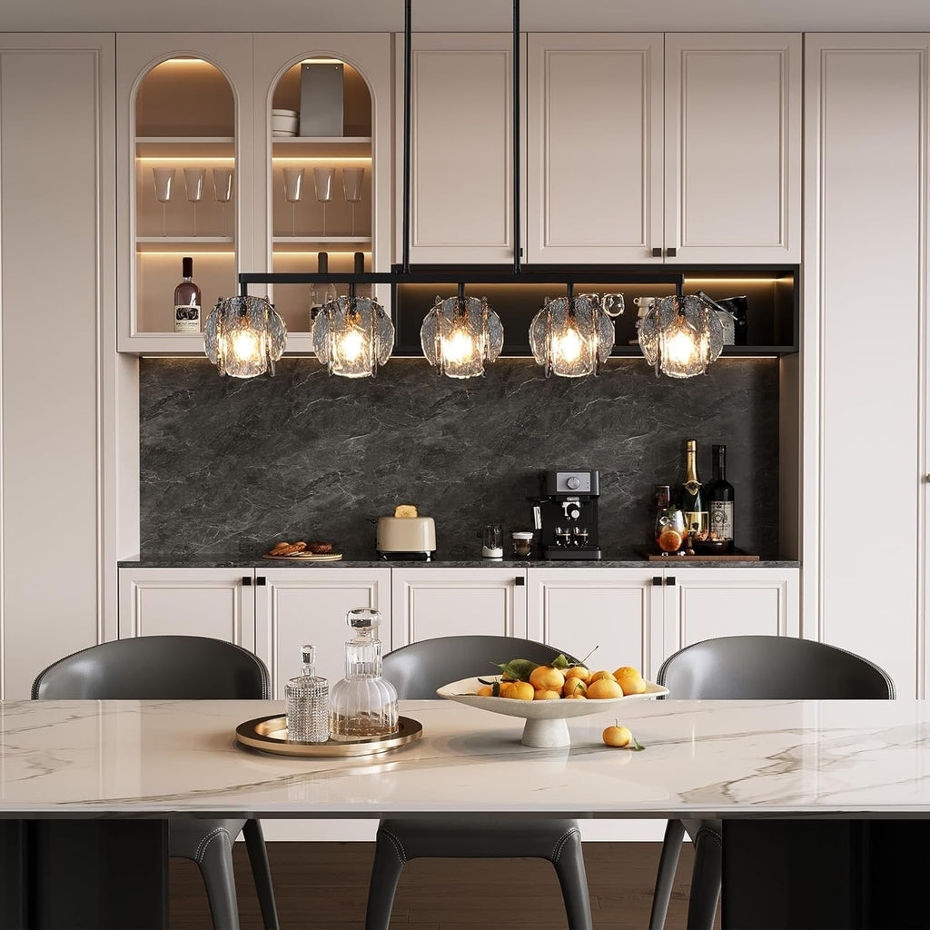 The chandelier lit above a marble island in a cream and black kitchen