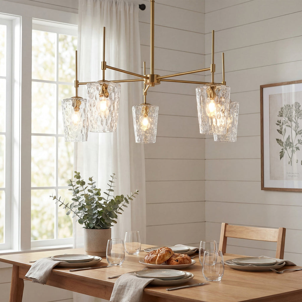 Five arm gold chandelier with hammered glass shades lit above a wooden dining table