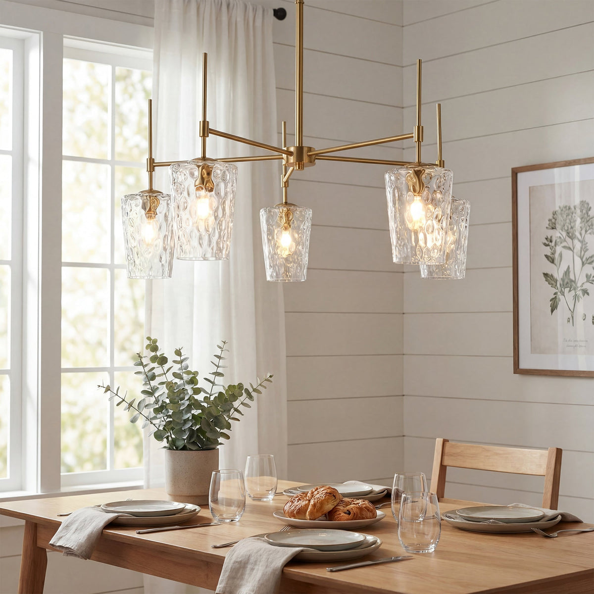 Five arm gold chandelier with hammered glass shades lit above a wooden dining table