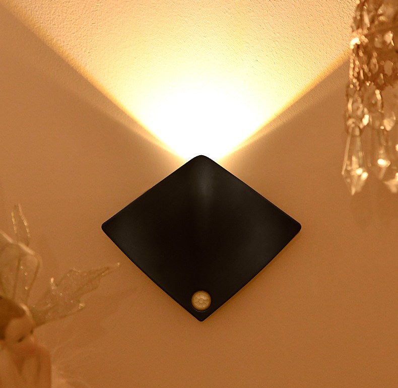 Warm uplight from a black sensor wall lamp on a hallway wall at night
