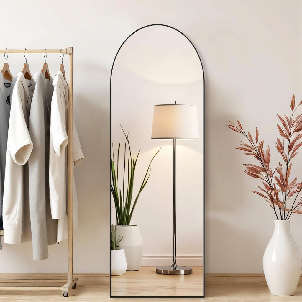 Black arched mirror leaning beside a clothes rail and floor lamp