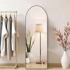 Black arched mirror leaning beside a clothes rail and floor lamp
