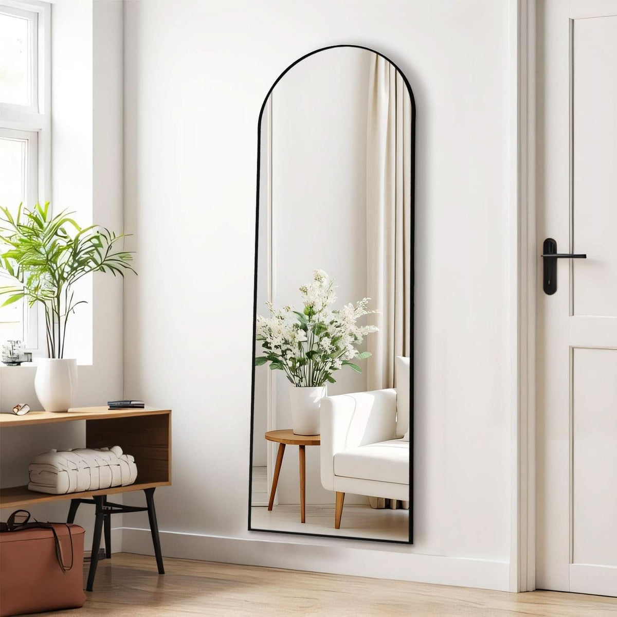 Arched full length mirror against a white wall beside a console table