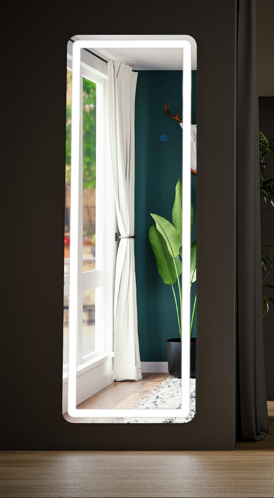 Rounded-corner LED full length mirror hung on a dark wall, reflecting a window, curtain and plant