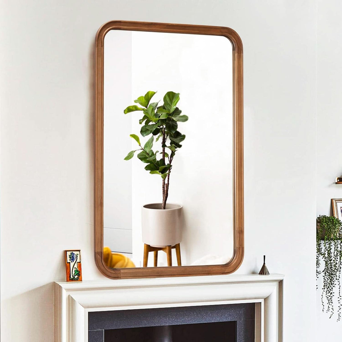 Wood framed mirror hung above a fireplace reflecting a plant