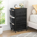 Stowena black 3 drawer nightstand with side pockets beside a bed with white bedding