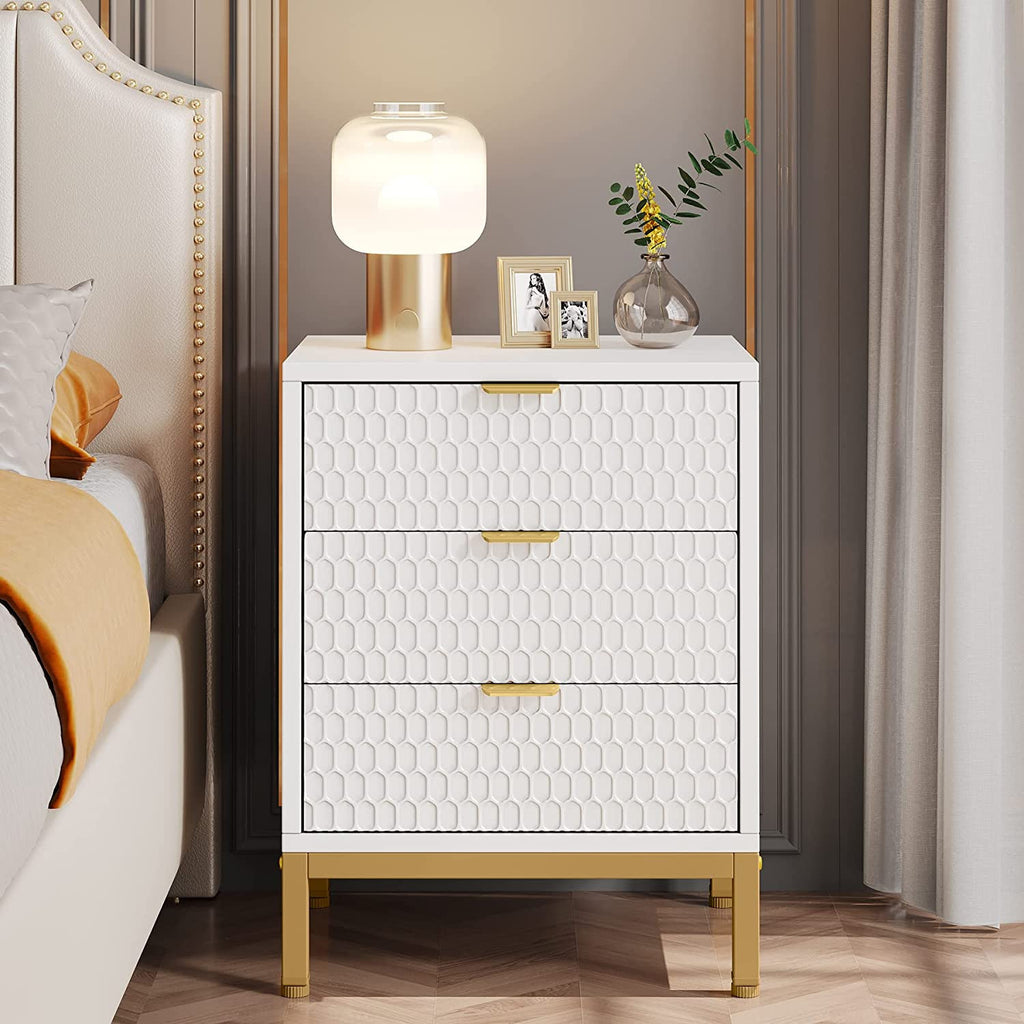 Tall white nightstand with honeycomb drawer fronts holding a gold lamp and framed photo