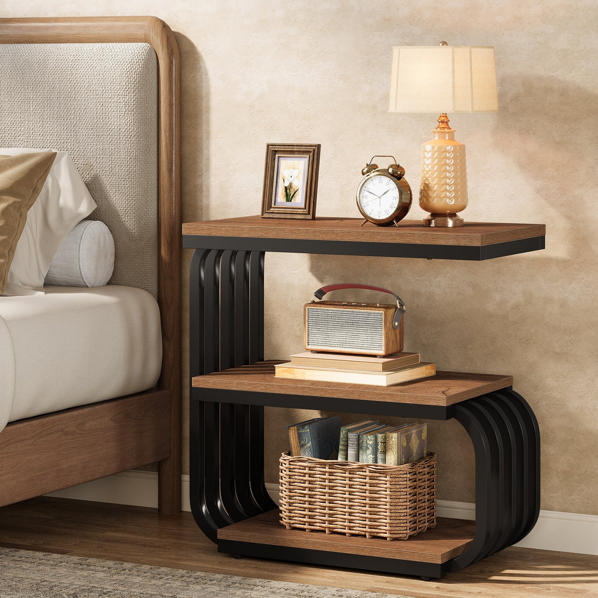 Stowena brown 3 tier narrow nightstand beside a bed with a lamp and books