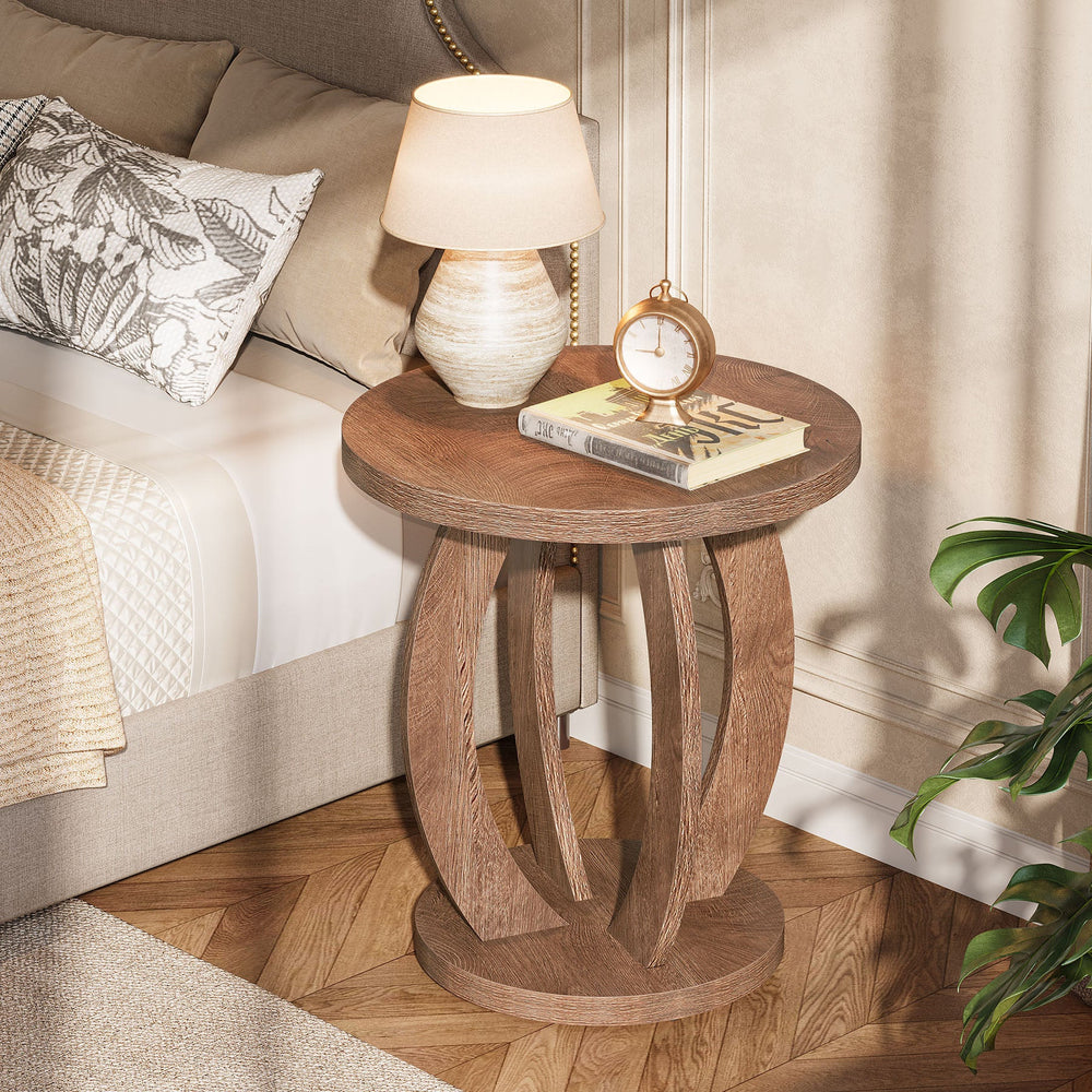 Round bedside table with lamp and books by a cream headboard