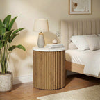 Ribbed base nightstand with lamp beside an upholstered bed